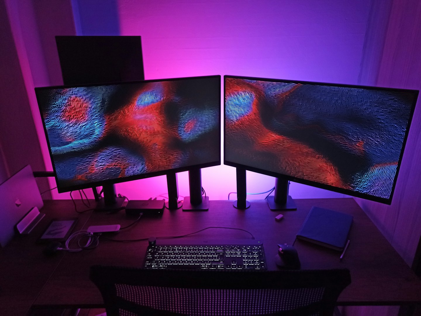 Postazione di lavoro con doppio monitor che mostra arte astratta.